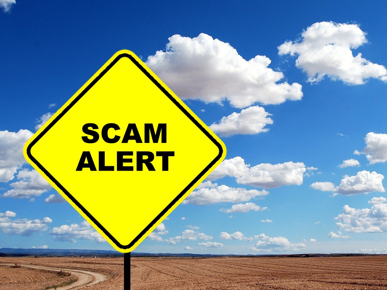 Yellow sign reading Scam alert against blue sky