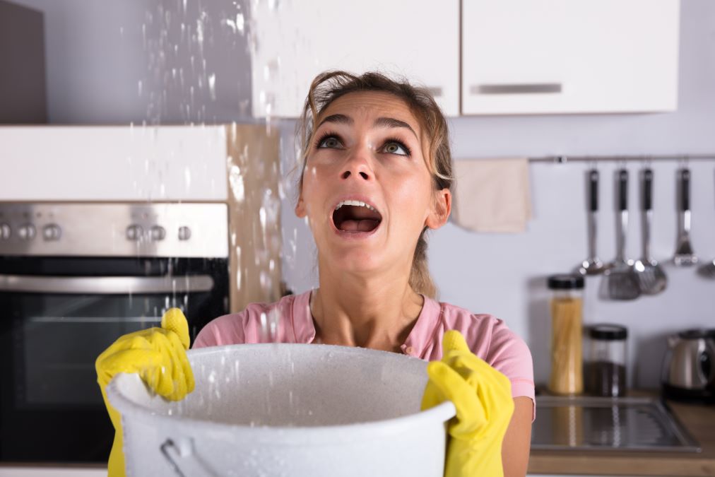 Woman holding a bucket while water droplets leak from ceiling